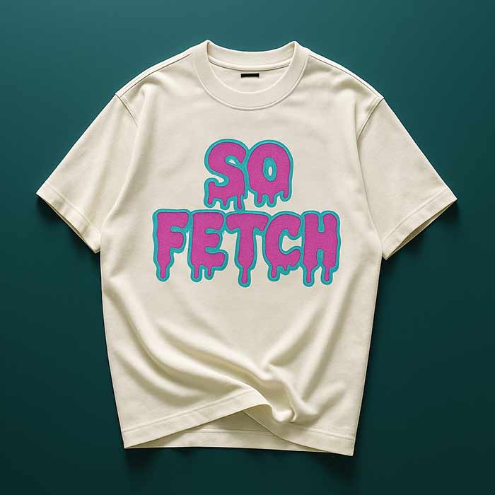 A cream-colored t-shirt featuring the phrase 'SO FETCH' in vibrant blue and pink dripping letters, laid flat against a dark green background.
