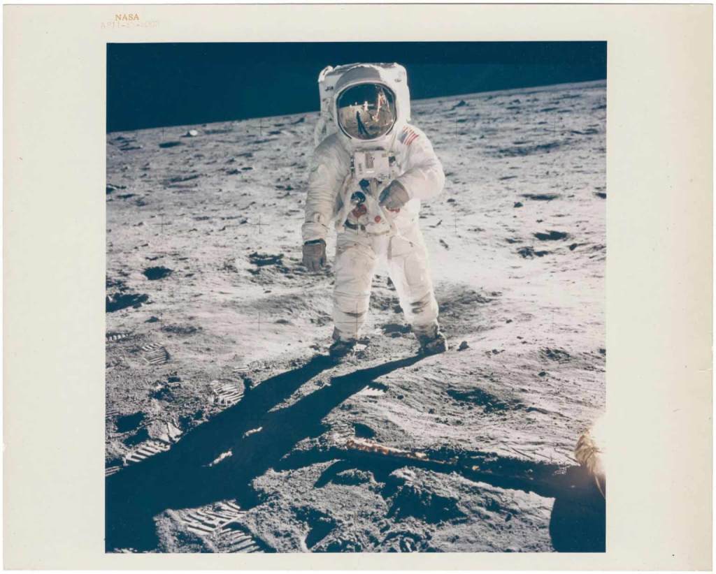 Astronaut standing on the surface of the Moon, wearing a space suit, with shadows cast on the lunar surface.
